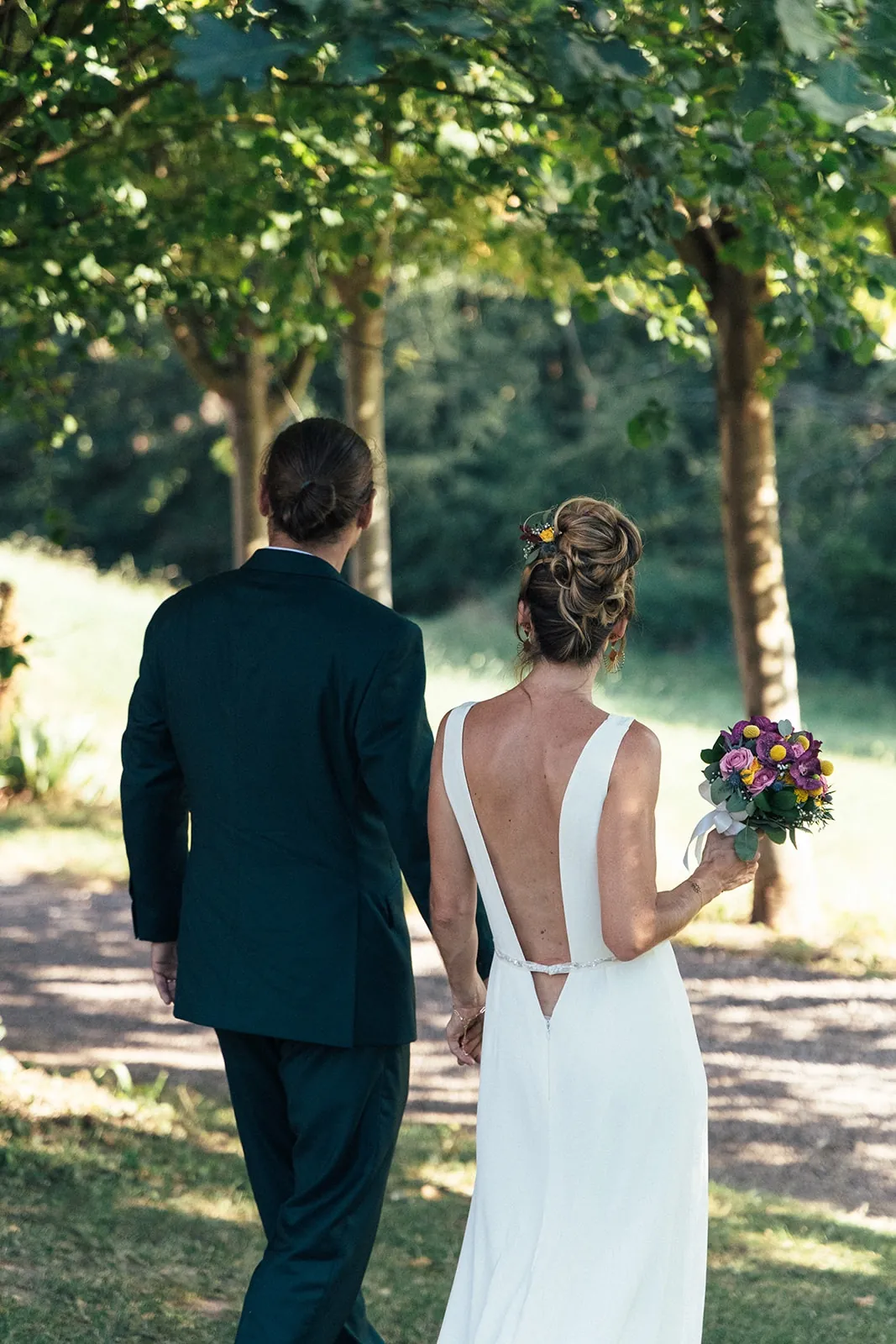 Caroline et son mari de dos dans l'allée, son bouquet coloré à la main : le dos ouvert de la robe