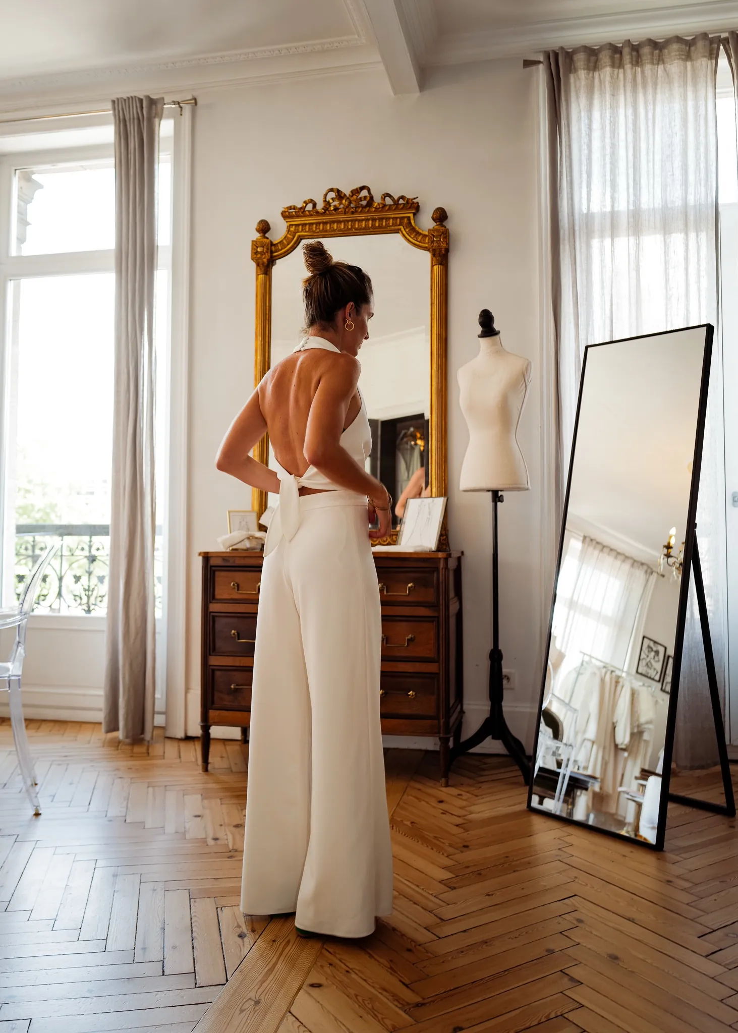 Caroline de dos devant le miroir doré du showroom : top dos nu noué dans le dos et pantalon large blanc