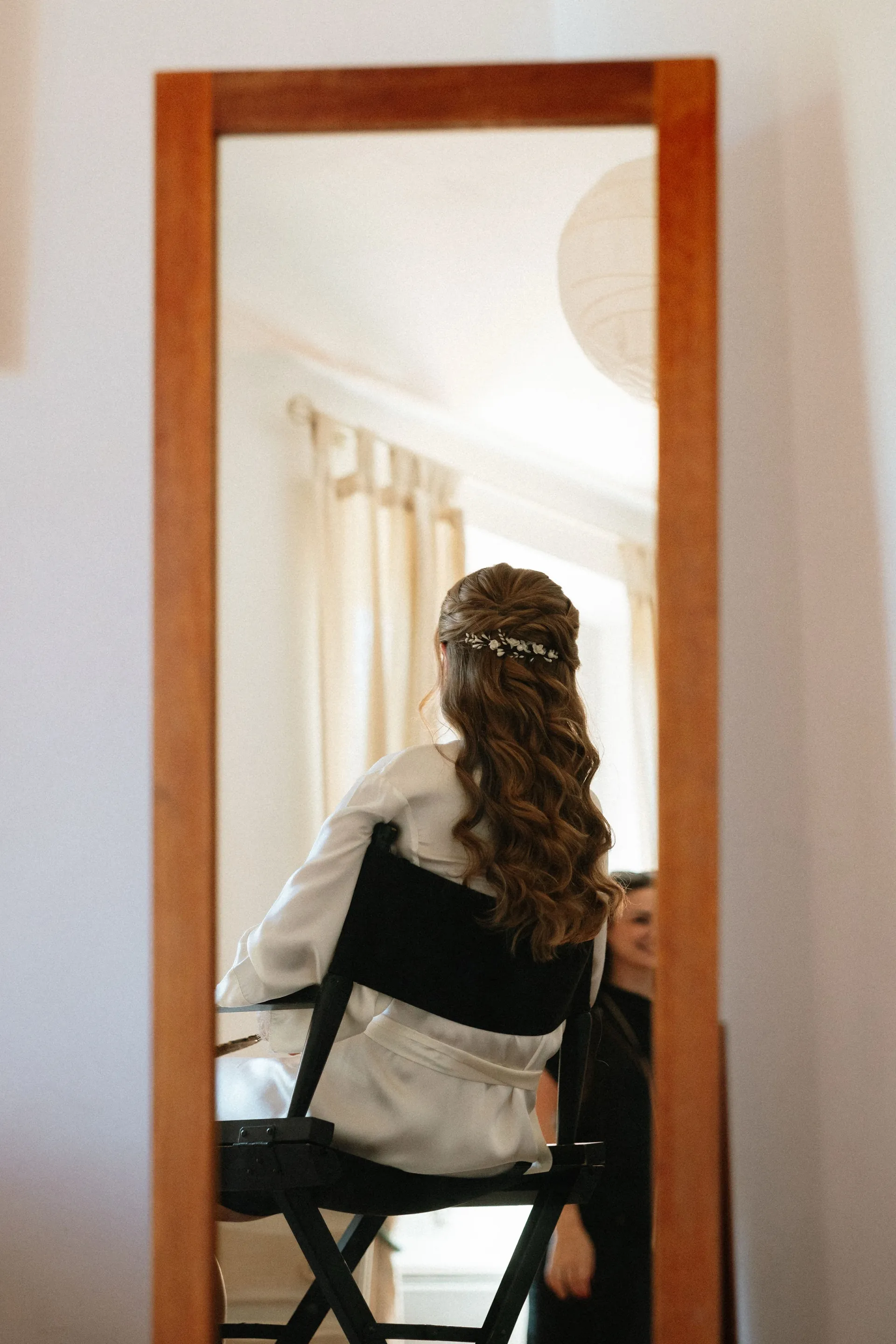 Eugénie de dos dans le miroir, assise sur une chaise de maquillage, un peigne dans les cheveux