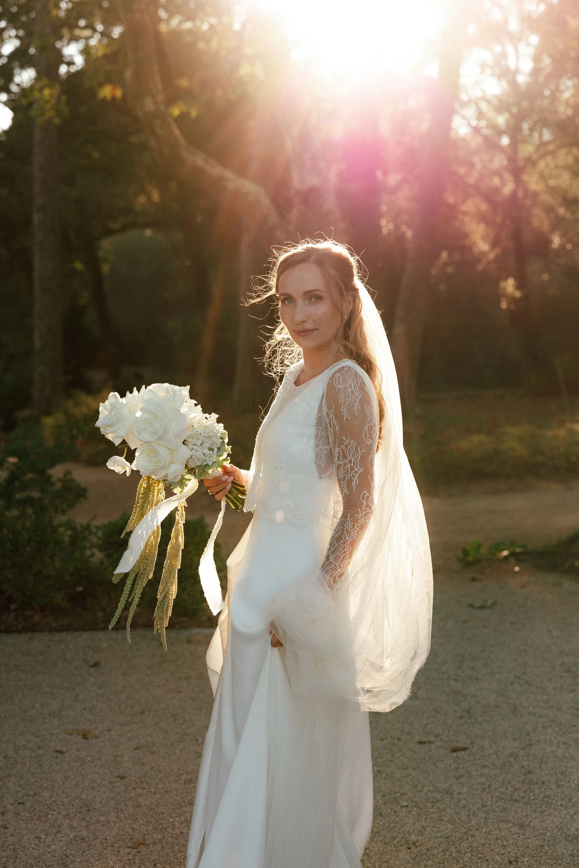 Eugénie, bouquet blanc à la main, dans la lumière dorée de fin de journée, son voile derrière elle