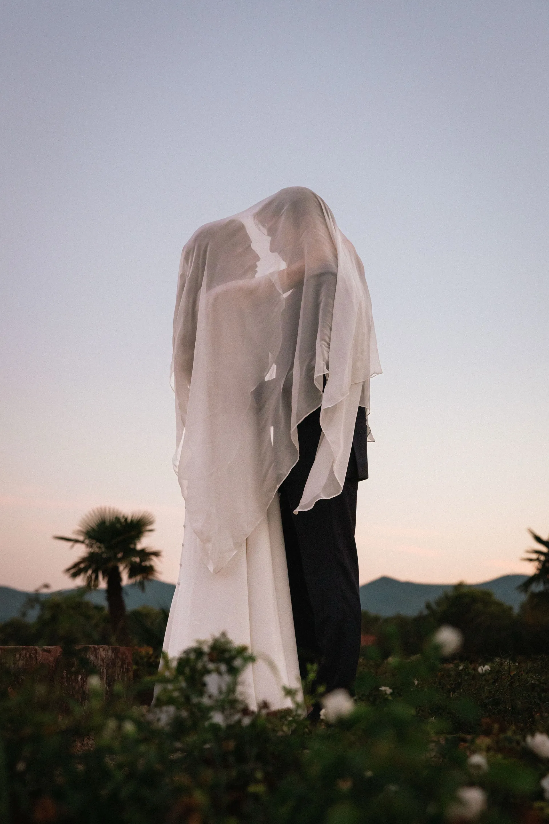 Le couple sous un voile léger, au crépuscule, entre les palmiers et les collines