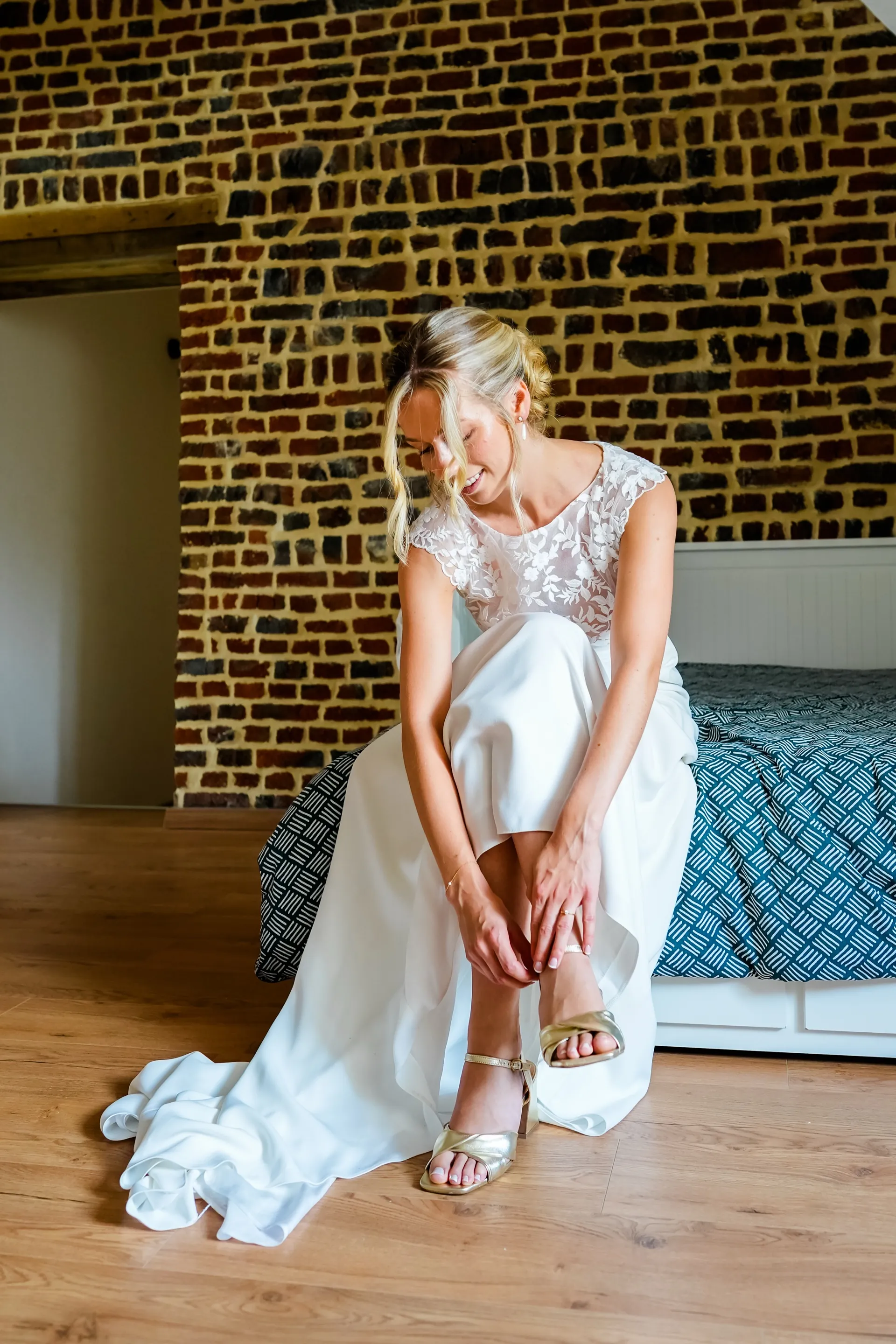 Lola, assise dans sa chambre, ajuste sa sandale : la jupe fluide de la robe LIYA retombe en traîne sur le parquet