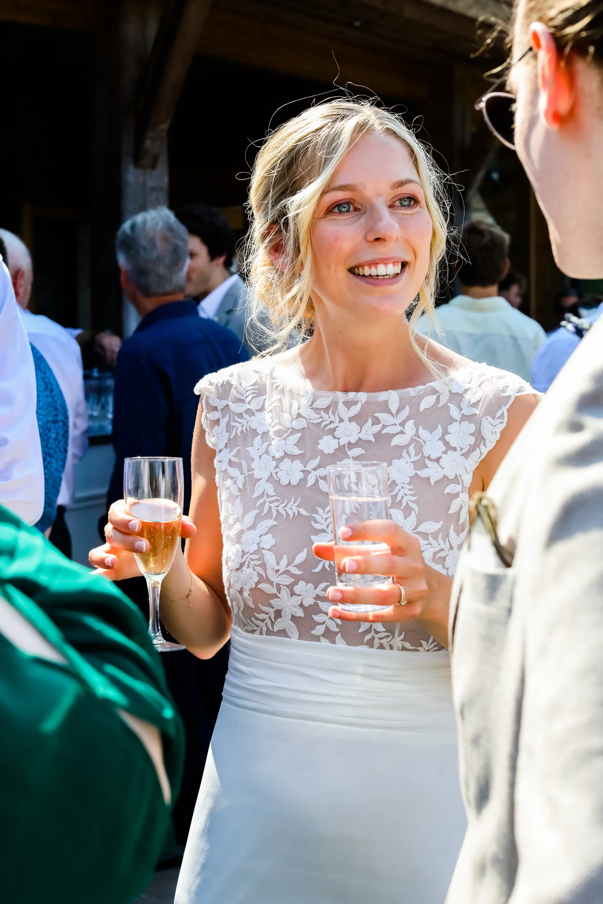 Lola, radieuse, une coupe de champagne à la main au milieu de ses invités : buste en tulle brodé de la robe LIYA