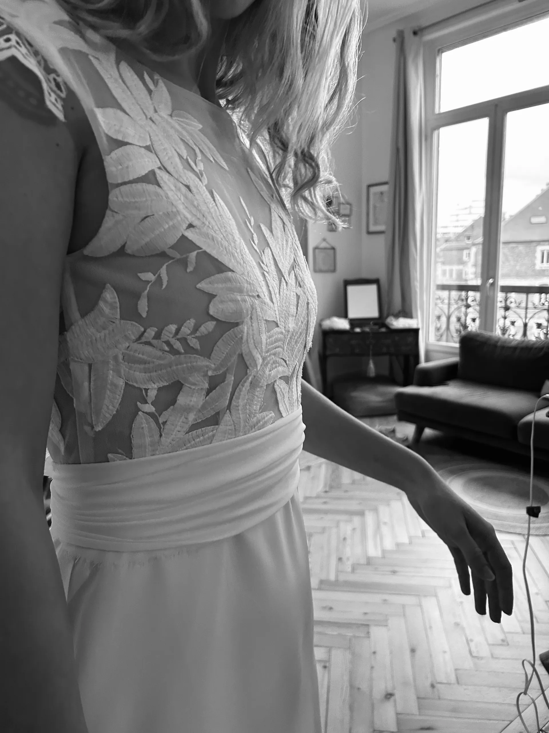 Le buste en tulle brodé de feuillages et la ceinture en mousseline plissée de la robe LIYA, en noir et blanc