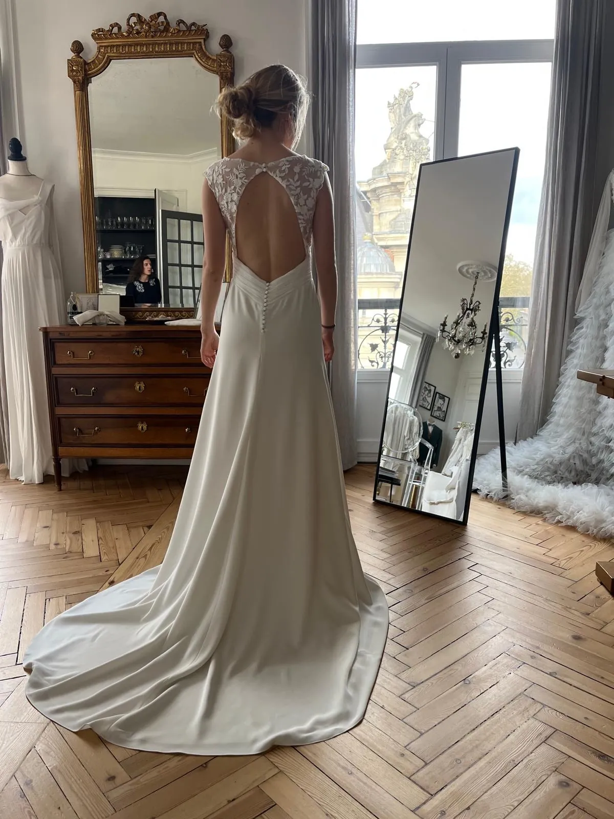 Le dos échancré, les petits boutons du bas du dos et la traîne de la robe LIYA, sur le parquet du showroom