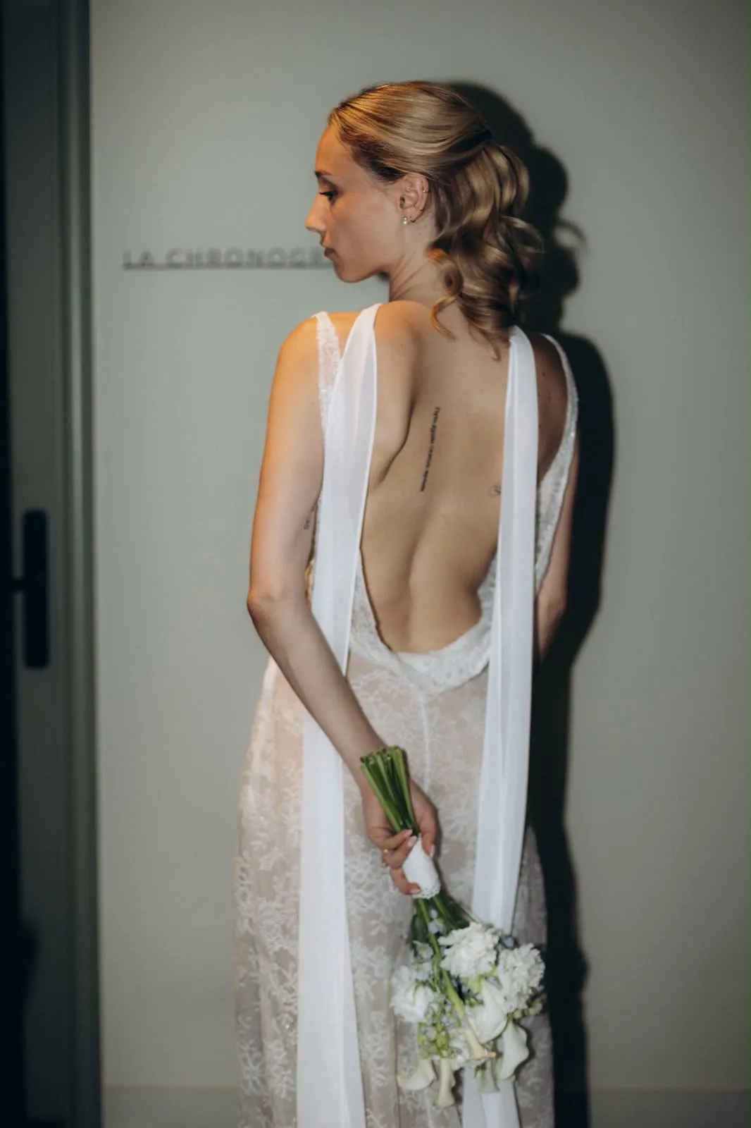 Marie de dos, le dos bénitier de la robe ALBA, son bouquet tenu dans le dos