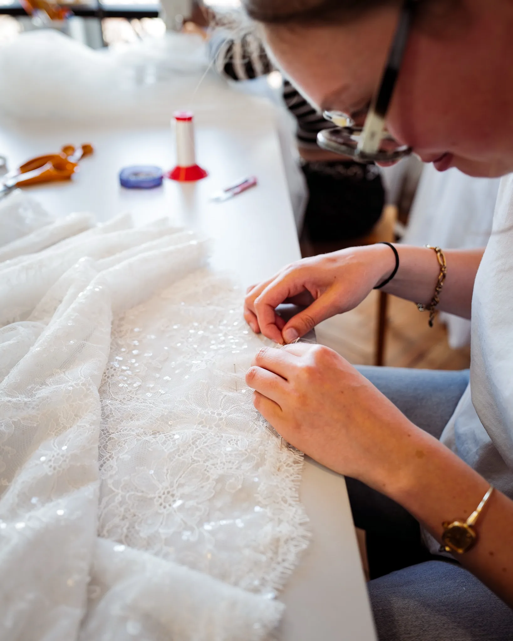 À l'atelier, la couturière travaille à la main les perles et la dentelle de la robe